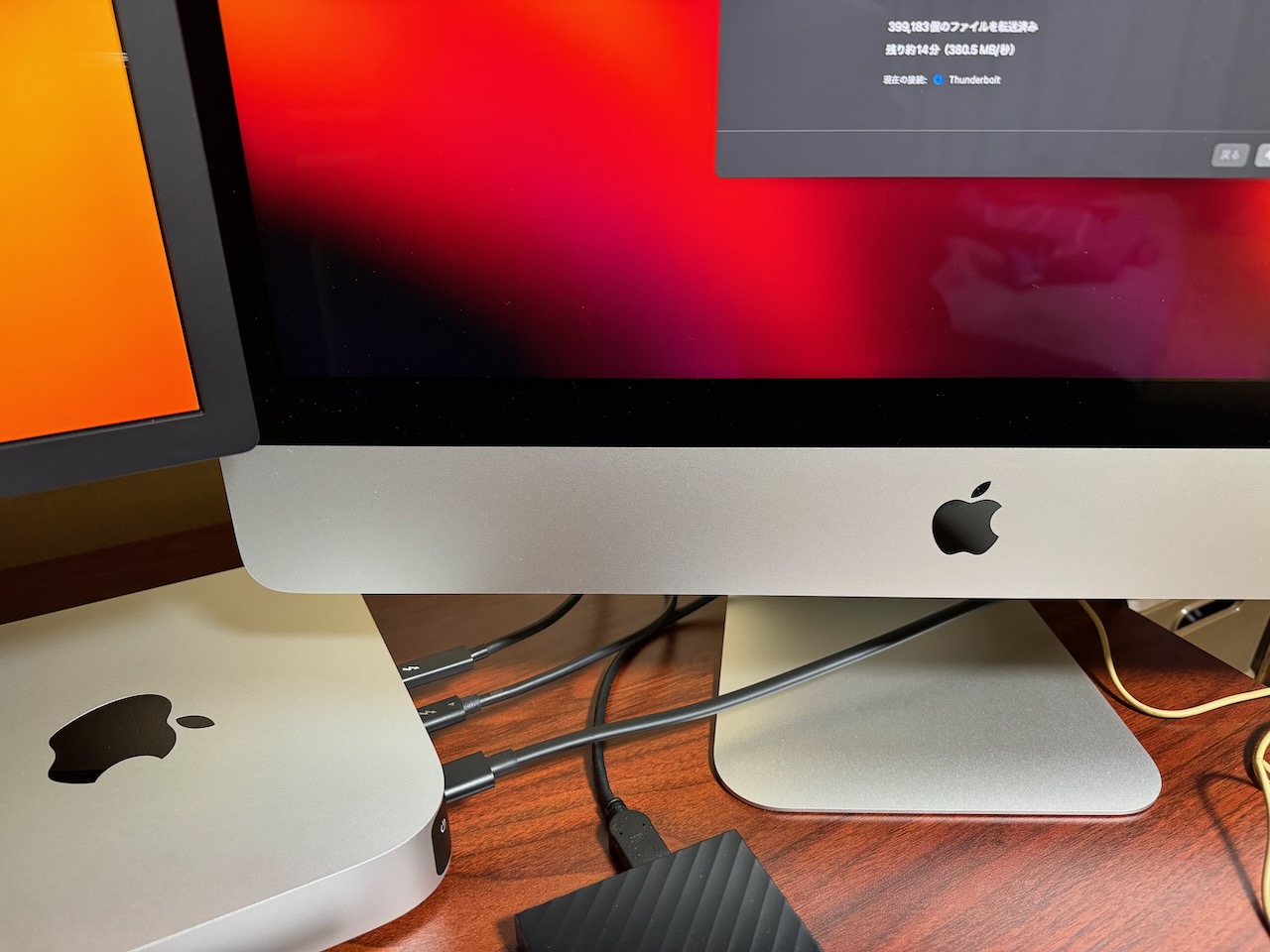 移行アシスタント実行中の写真。2台のMacは中央のThunderbolt 4ケーブルで直接つながっている。iMacの画面には転送時間が「残り14分」と表示されている。